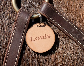 May include: Close-up of a brown leather horse halter with a brown leather tag that says "Louis" on it.