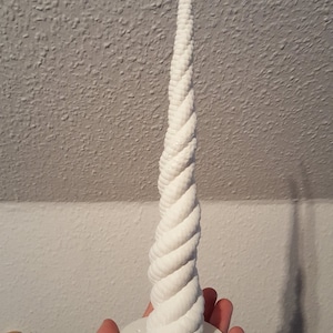 May include: A white 3D printed unicorn horn with a spiral design. The horn is on a white base with small holes.
