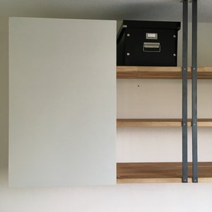 May include: A white cabinet with two wooden shelves and black metal supports. A black box is on the top shelf.