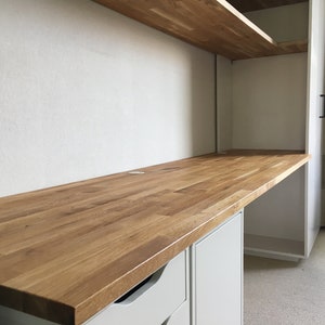 May include: A light wood desk top with a white cabinet underneath. The desk top is made of wood planks and has a smooth finish. The cabinet has two drawers and a door.