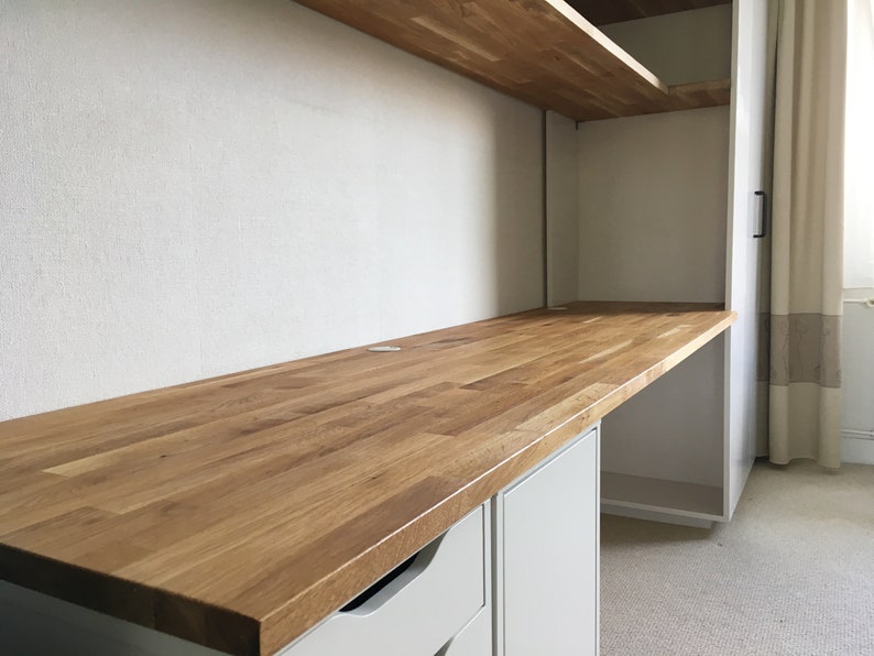 May include: A light wood desk top with a white cabinet underneath. The desk top is made of wood planks and has a smooth finish. The cabinet has two drawers and a door.