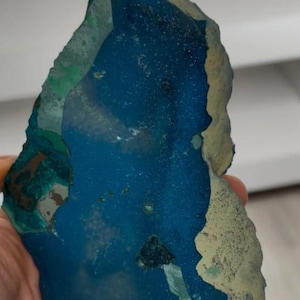 May include: A vibrant, irregularly shaped stone with a deep blue center, edged with a lighter, textured border. Patches of green and tan hues add to the natural, raw aesthetic of this unique mineral specimen.