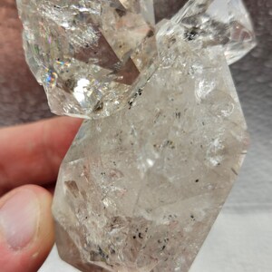 May include: A clear quartz crystal cluster with multiple points and a rough, textured surface. The crystal has a slight iridescent sheen.