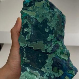 May include: A large, irregular mineral specimen featuring a vibrant mix of deep navy blue, forest green, and bright turquoise patches. The surface displays a varied, layered texture with smooth and matte sections across the entire rock formation.
