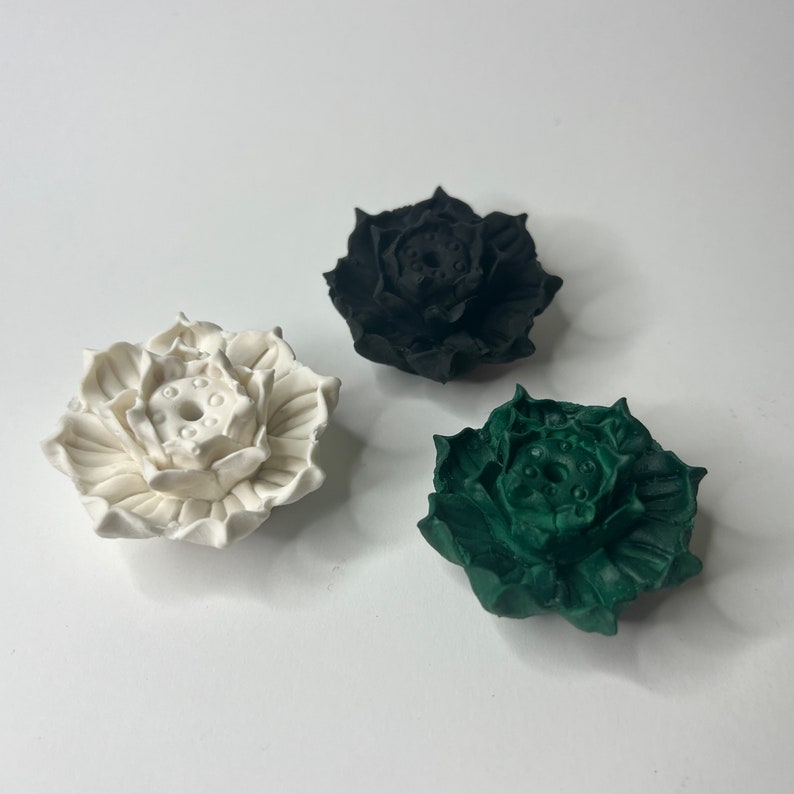 Puede incluir: Tres esculturas decorativas de flores de loto en blanco, negro y verde. Las esculturas tienen dise&ntilde;os detallados de p&eacute;talos y una c&aacute;psula central de semillas. Los objetos est&aacute;n dispuestos sobre una superficie blanca, mostrando el contraste de colores y texturas.