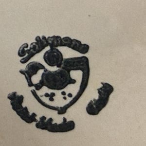 May include: A black, stylized emblem with the word "Collingwood" arched above a central design. The design includes a shield shape with a bird-like figure and several small dots. The emblem is on a cream-colored background.