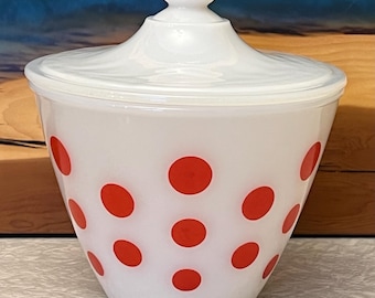 May include: White glass jar with a lid, adorned with large red polka dots. The jar has a rounded shape and a matching white lid with a small knob. A vintage-style kitchen storage container.