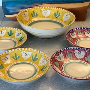 May include: A collection of ceramic bowls with hand-painted designs. The bowls feature a yellow or burgundy rim with white bird and green leaf motifs. The bowls vary in size, with the largest measuring approximately 10 inches in diameter.
