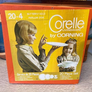 May include: A vintage Corelle Livingware 20-piece dinnerware set in the Butterfly Gold pattern. The box shows a woman and a girl holding plates and bowls. The set includes dinner plates, luncheon plates, bowls, and cups with saucers.