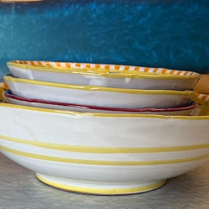 May include: A white ceramic mug with a black handle and the text "But first, coffee" in a black, handwritten-style font. The mug is on a white surface.