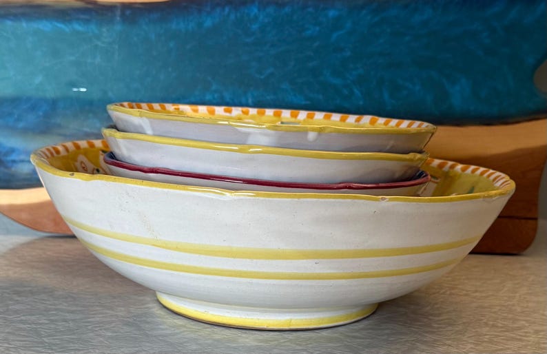 May include: A white ceramic mug with a black handle and the text "But first, coffee" in a black, handwritten-style font. The mug is on a white surface.