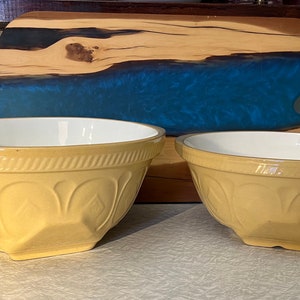 May include: Two yellow ceramic mixing bowls with a white interior. Each bowl features a textured exterior with a repeating embossed pattern around the rim and a series of arched indentations along the sides, creating a classic kitchen aesthetic.