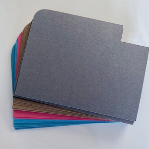 May include: A stack of colorful paper folders with rounded corners. The top folder is gray, the next is brown, then pink, and finally blue.