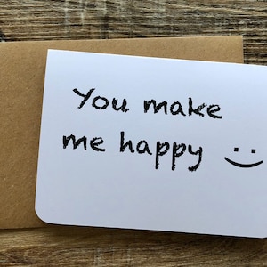May include: A white card with black handwritten text that says "You make me happy" and a simple smiley face.