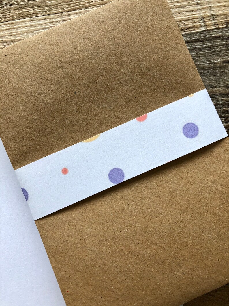 May include: A brown paper envelope with a white strip of paper adhered to the bottom edge. The white paper has a repeating pattern of small purple, orange, and yellow circles.
