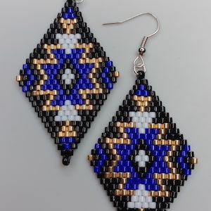 May include: A pair of beaded earrings with a diamond shape. The earrings feature a pattern of black, blue, gold, and white beads. The ear wires are silver-colored.