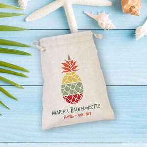 May include: A white drawstring bag with a colorful pineapple design and the text "Maria's Bachelorette Florida - June, 2019".