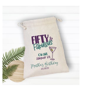 May include: A white fabric drawstring bag with the text "FIFTY & Fabulous" in purple and green lettering. The bag also includes the text "Oh Shit Hangover Kit Martha's Birthday 05.30.22" in black lettering.