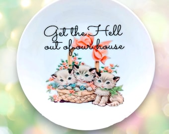 May include: White ceramic plate with a vintage illustration of three kittens in a basket with flowers. The plate has the text "Get the Hell out of our house" in black script.