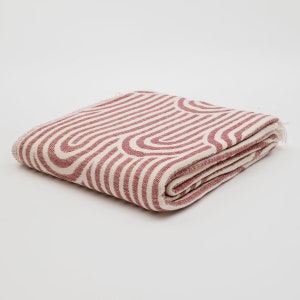 May include: A folded pink and white striped throw blanket with a geometric pattern. The blanket is made of a soft, woven fabric.