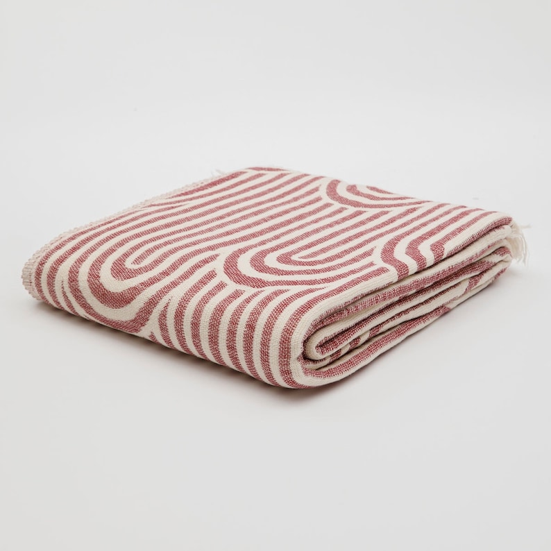 May include: A folded pink and white striped throw blanket with a geometric pattern. The blanket is made of a soft, woven fabric.