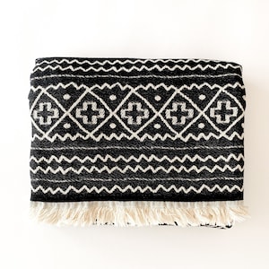 May include: Black and white throw blanket with a geometric pattern and fringe trim.