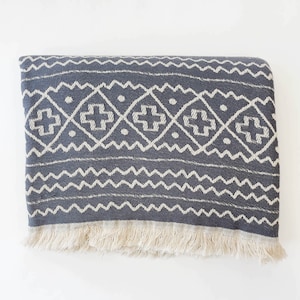 May include: A gray and white patterned throw blanket with fringe. The blanket has a geometric design with white diamonds and crosses on a gray background.
