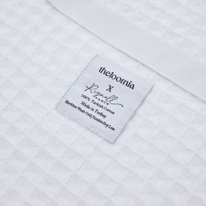 May include: White label with black text that reads "theloomia" and "Rignell Ranch" with the text "X" between the two names. The label also includes the text "100% Turkish Cotton", "Made in Turkey", and "Machine Wash Cold, Tumble Dry Low".