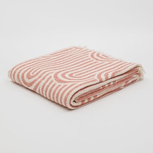May include: A folded pink and white throw blanket with a geometric pattern of curved lines. The blanket has a fringed edge.