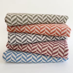 May include: A stack of five woven blankets with a chevron pattern. The blankets are in various colors, including green, orange, black, burgundy, and blue.