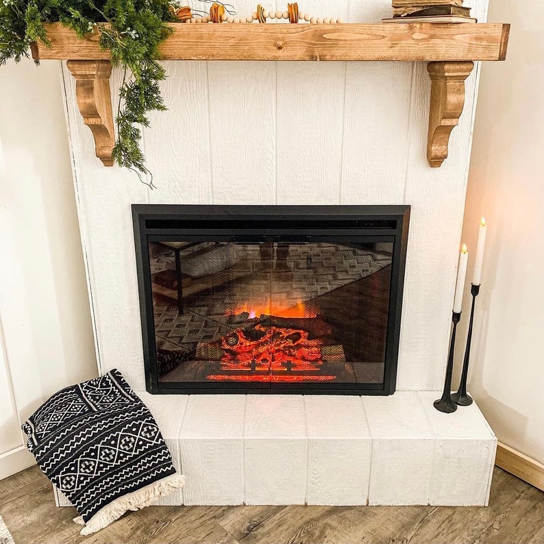 May include: A white fireplace mantel with a black electric fireplace insert. The fireplace is lit and has a realistic flame effect. The mantel is decorated with a wooden shelf and a row of wooden beads.