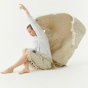 May include: A woman sits on a beige and brown striped throw blanket with fringe. The blanket has a wavy pattern.