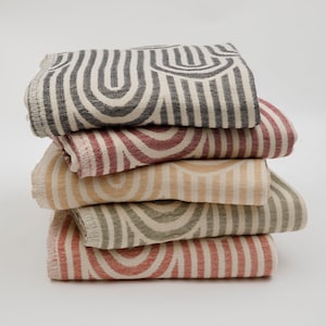May include: A stack of five woven cotton throw blankets with a geometric pattern of black, red, beige, and green stripes and arches.