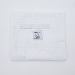 May include: White waffle weave kitchen towel with a label that reads "theloomia x Regull, 100% Turkish Cotton, Made in Turkey, Machine Wash Cold, Tumble Dry Low."