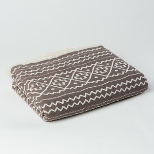 May include: A brown and white patterned throw blanket with a fringe border.