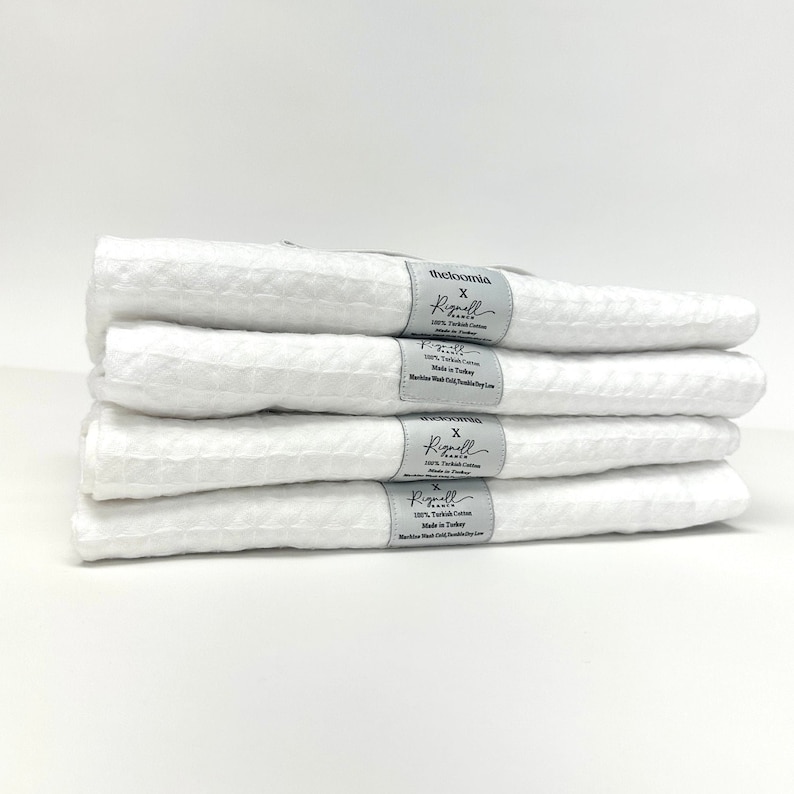 May include: A stack of five white waffle weave kitchen towels with a gray label that reads "theloomia x Rignell Home 100% Turkish Cotton Made in Turkey Machine Wash Cold Tumble Dry Low"