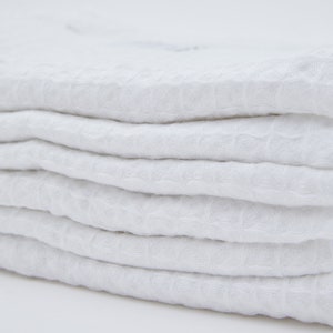 May include: A stack of white waffle weave kitchen towels. The towels are folded neatly and have a soft, textured surface.