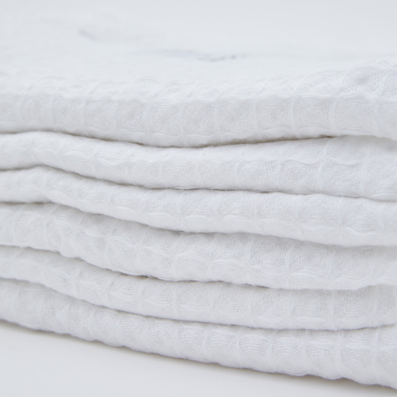 May include: A stack of white waffle weave kitchen towels. The towels are folded neatly and have a soft, textured surface.