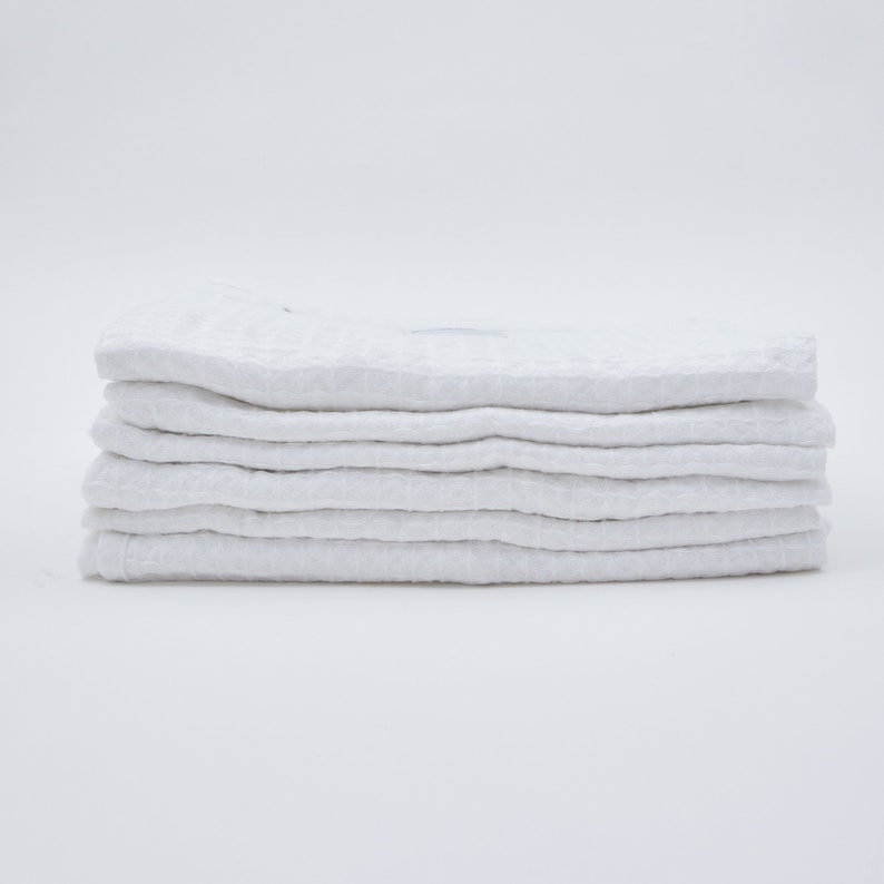 May include: A stack of six white waffle weave kitchen towels.