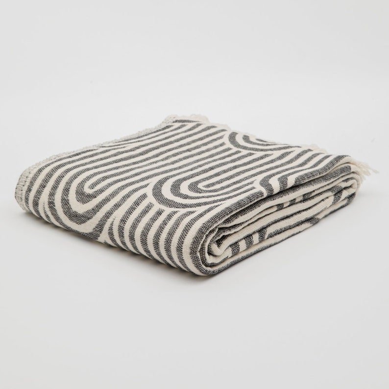 May include: A folded white and gray striped throw blanket with a geometric pattern. The blanket is made of a soft, woven fabric.