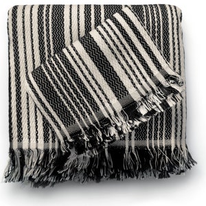 May include: A folded black and white striped throw blanket with a matching smaller blanket on top. The blankets have a fringe trim on the edges. The pattern is a mix of vertical stripes and a zig-zag design.