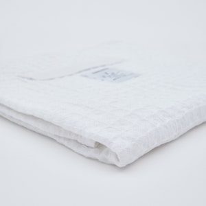 May include: A white, textured, cotton towel folded in half. The towel is made of a soft, absorbent material.