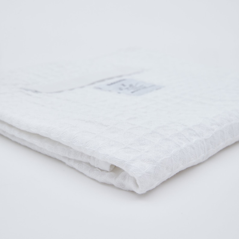 May include: A white, textured, cotton towel folded in half. The towel is made of a soft, absorbent material.
