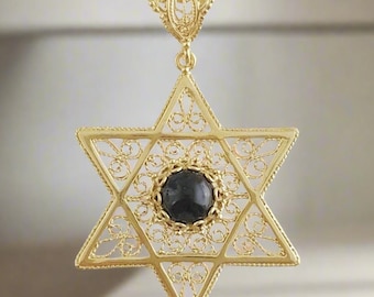 Peut inclure: Un pendentif en or en forme d'étoile de David avec une pierre précieuse noire au centre. Le pendentif est en filigrane et a un design délicat.