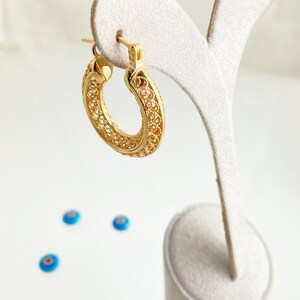 May include: Gold filigree hoop earrings with a delicate, intricate design. The earrings are displayed on a white stand.