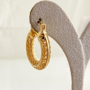 May include: Gold filigree hoop earrings. The earrings are made of delicate, intricate metalwork and have a circular shape.