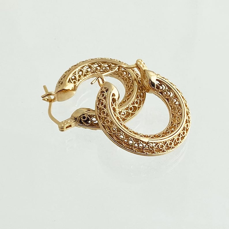 May include: Gold filigree hoop earrings. The earrings are made of delicate, intricate metalwork and have a circular shape.