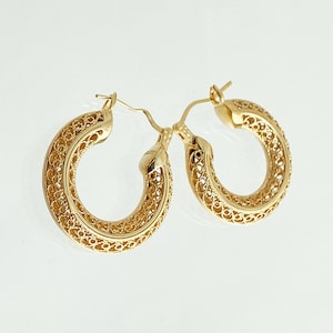 May include: A pair of gold hoop earrings with a delicate filigree design. The earrings are made of a thin, intricate metalwork that creates a delicate and feminine look.