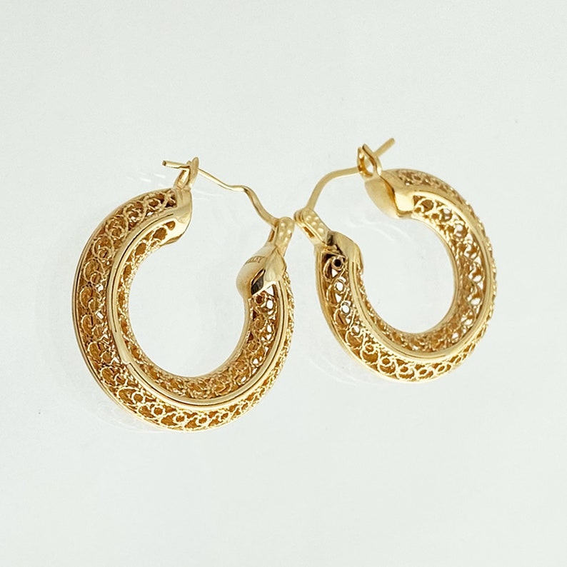 May include: A pair of gold hoop earrings with a delicate filigree design. The earrings are made of a thin, intricate metalwork that creates a delicate and feminine look.