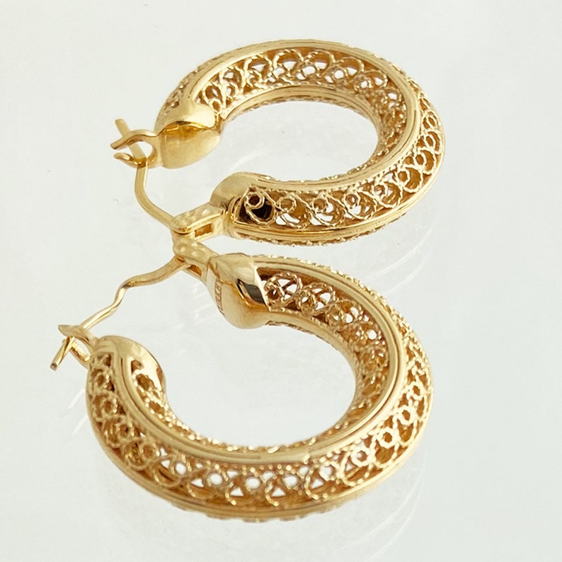 May include: Gold filigree hoop earrings with a delicate, intricate design. The earrings are made of a thin, lightweight metal and have a polished finish.